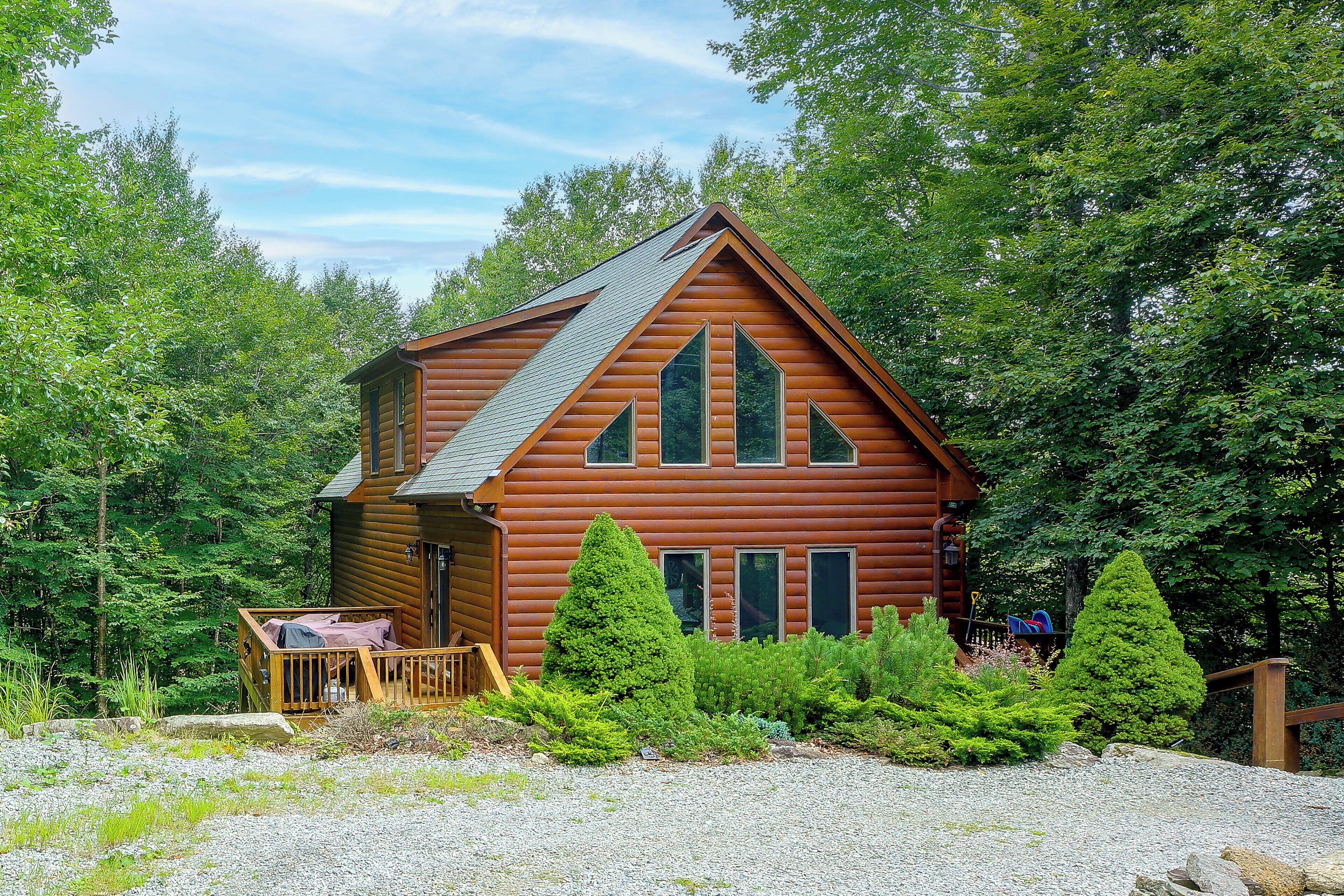 A log cabin with a porch, surrounded by dense greenery.