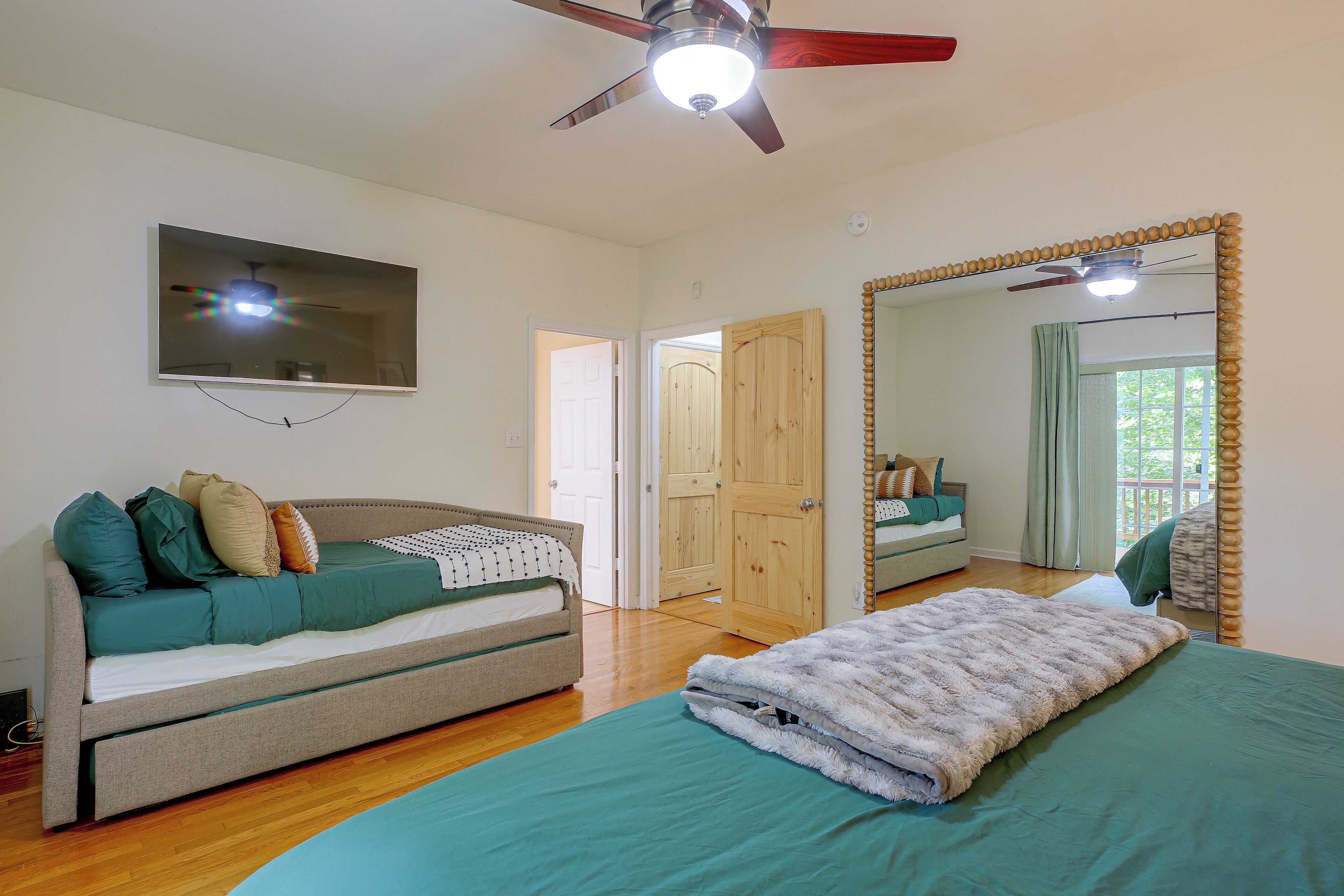 A bedroom with a bed, a sofa, a television, and a ceiling fan.