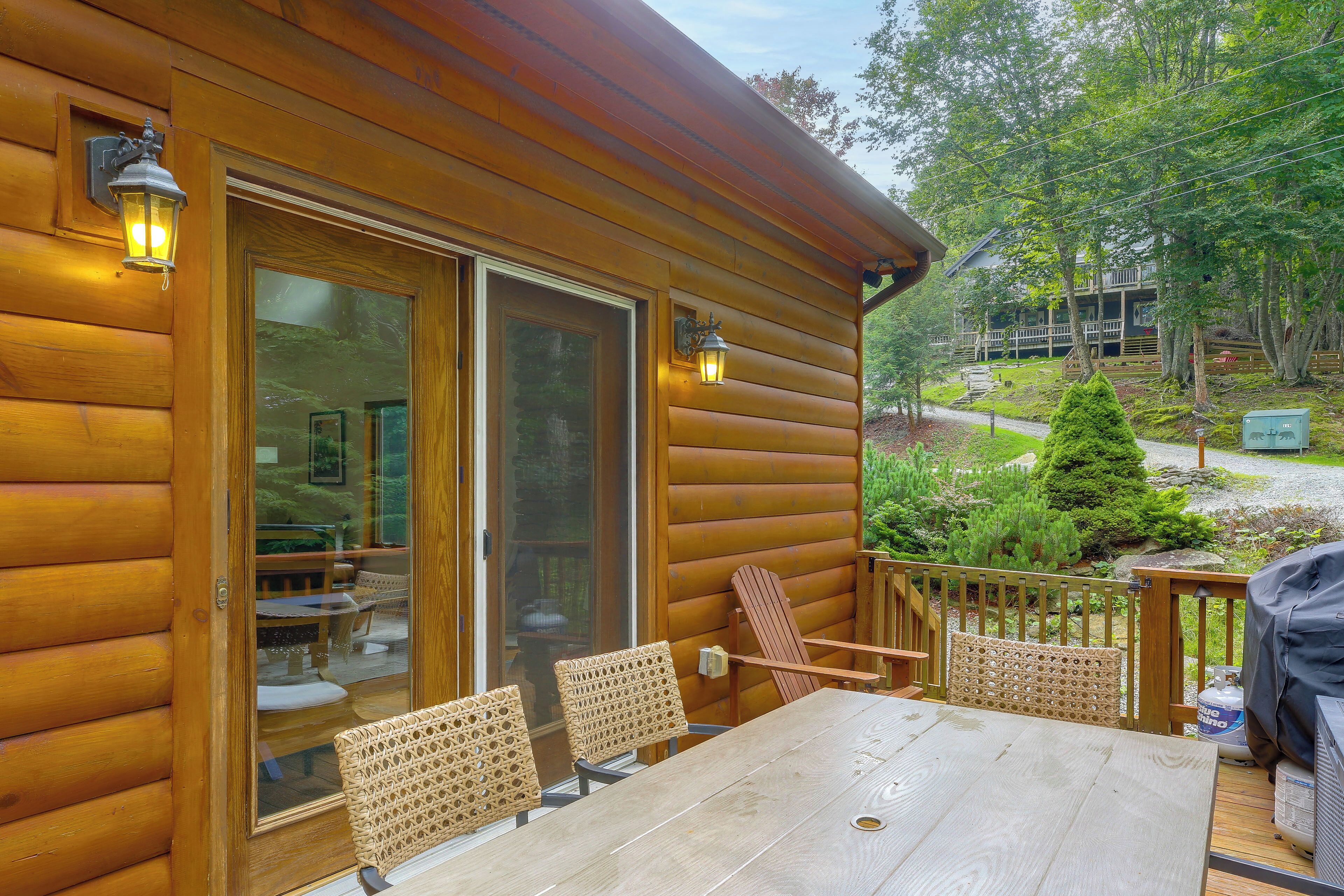 A wooden cabin with a deck, outdoor seating, and a view of a forested area.