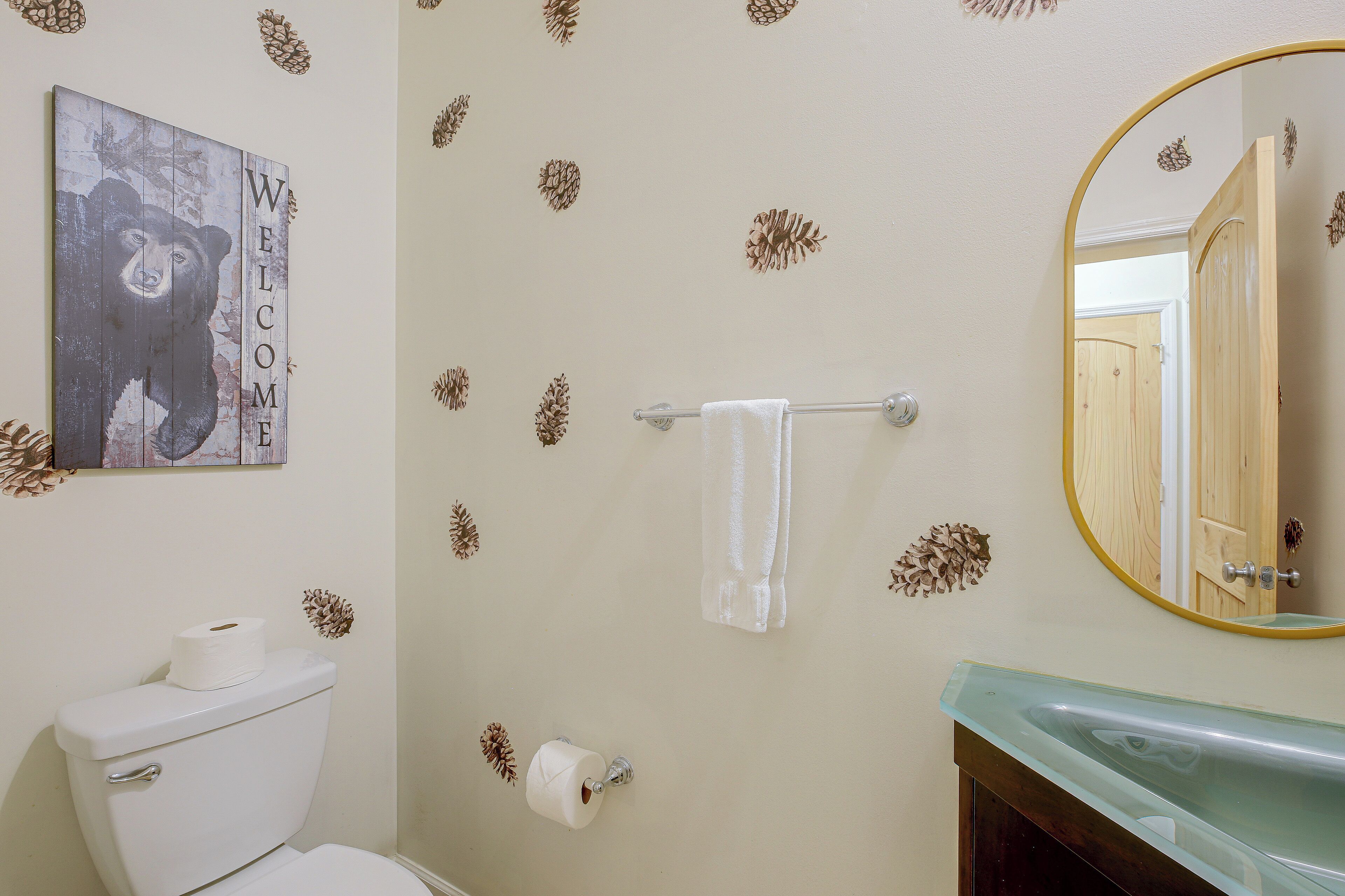 A bathroom with a toilet, a towel rack, a mirror, and a wall with a pinecone pattern.
