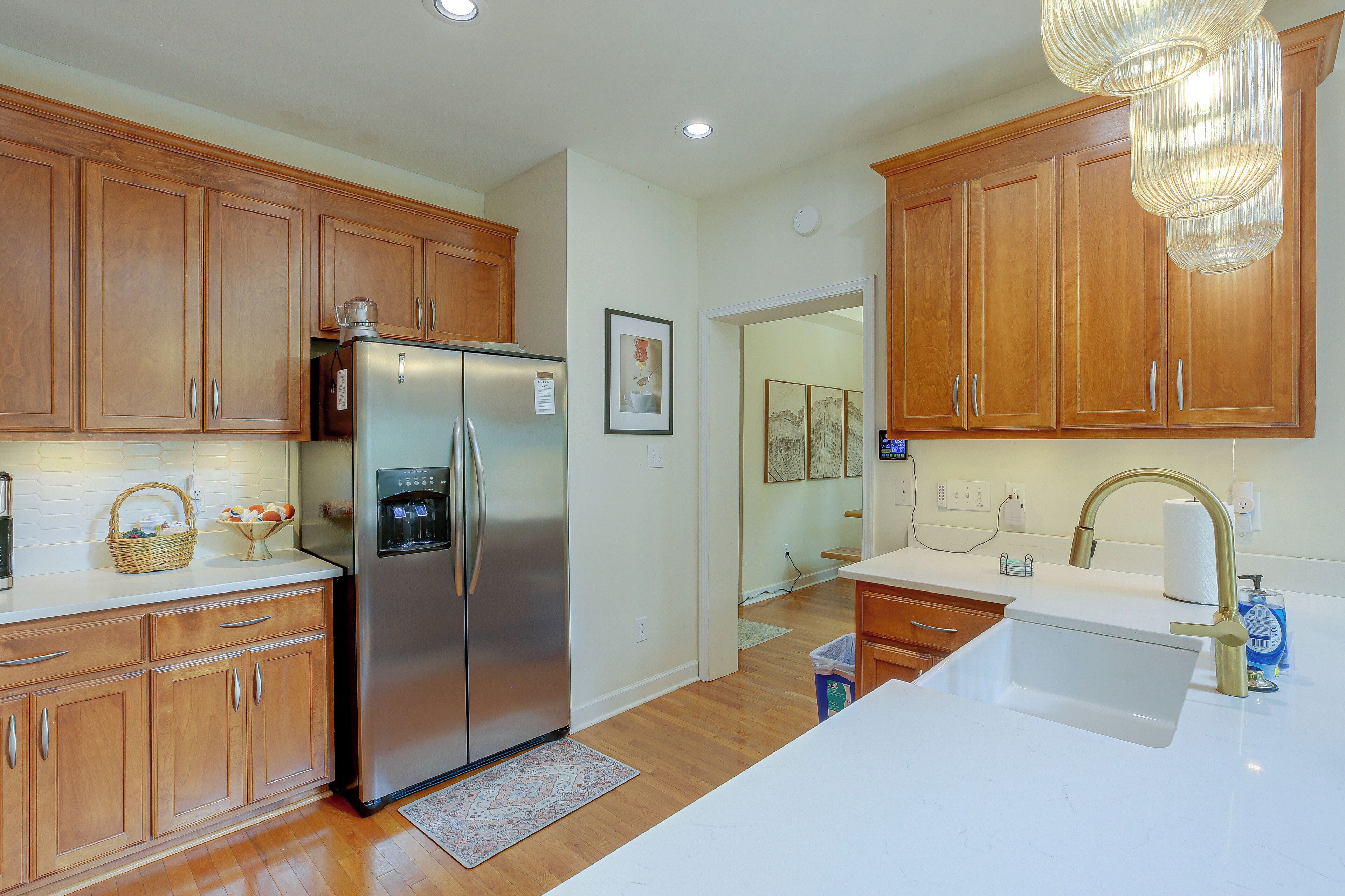 A kitchen with wooden cabinets, a stainless steel refrigerator, a sink with a gold faucet, and a chandelier.