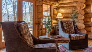 A log cabin interior with two leather armchairs, a small table, and a lamp.