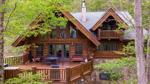 A log cabin with a deck, large windows, and a chimney.