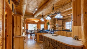 A rustic cabin interior with wooden walls, a stone counter, and a dining area with a large window.