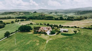Ländliche Landschaft mit sanften Hügeln, einem Bauernhof und wolkenlosem Himmel.