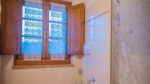 Ein Badezimmer mit Toilette, Badewanne, einem Fenster mit Spitzenvorhängen und einem Holzschrank.