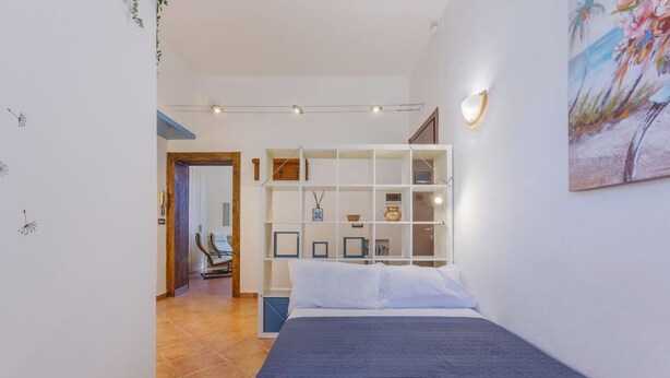 A bedroom with a bed, a white shelving unit, a painting, and a door leading to another room. - GuestHost - Ferrara Station Essential Apartment w/parking (Ferrara)
