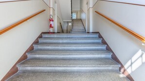 A staircase with wooden handrails, a fire extinguisher on the left, and a light fixture at the top. - GuestHost - Ferrara Station Essential Apartment w/parking (Ferrara)