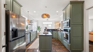 Uma cozinha moderna com armários verdes, eletrodomésticos de aço inoxidável e uma ilha central.