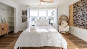 Quarto com uma cama grande, um ventilador de teto, uma cadeira de vime e vista para o exterior.