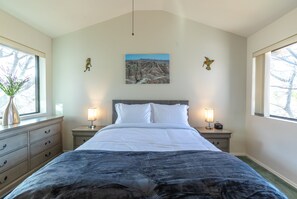 Une chambre avec un grand lit, deux tables de chevet avec des lampes, un tableau au mur et une fenêtre sur le côté gauche.