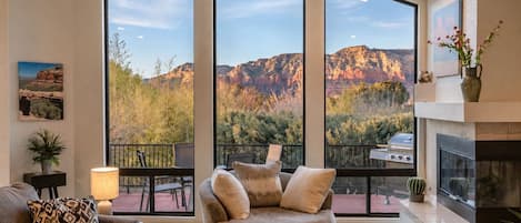 A spacious living room with a large window overlooking a mountainous landscape, a fireplace, and a comfortable seating area.
