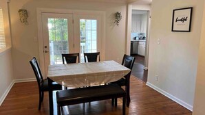 Un coin repas avec une table dressée pour quatre personnes, entourée de chaises, dans une pièce au plancher en bois et dotée d’une porte donnant sur la cuisine.