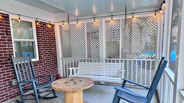 Une terrasse couverte avec une table en bois et deux fauteuils à bascule, un banc blanc et un paravent à treillis.