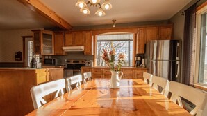 A kitchen with wooden cabinets, a stainless steel refrigerator, a dining table with chairs, and a window with a view of trees. - Les Chalets Tourisma - La Campagnarde (Saint-Leonard-de-Portneuf)