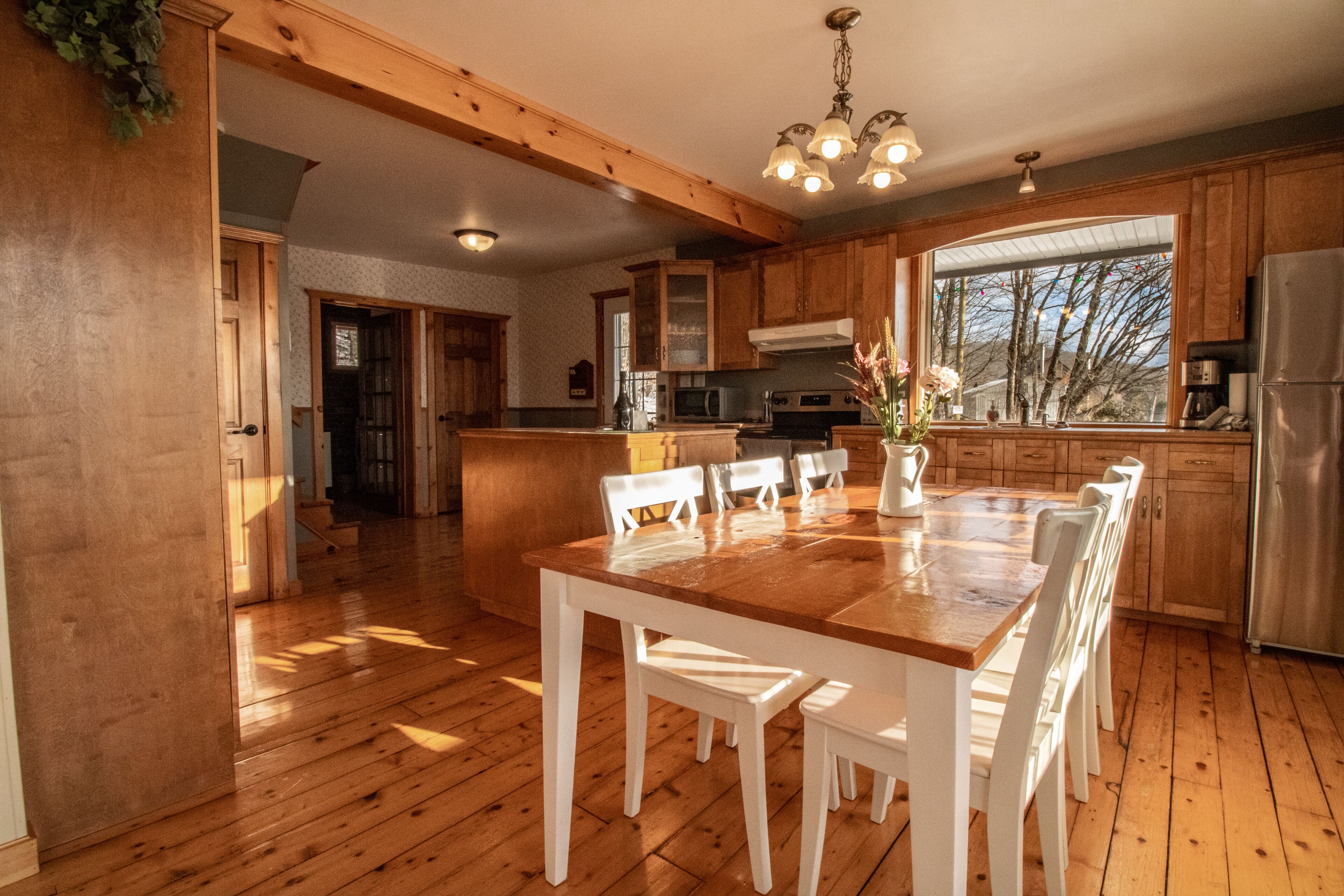 Una cocina amplia con armarios de madera, una isla central y un comedor con sillas blancas.