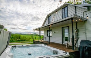 Ein Haus mit Whirlpool auf der Terrasse, einer überdachten Veranda und Blick auf eine grüne Landschaft.