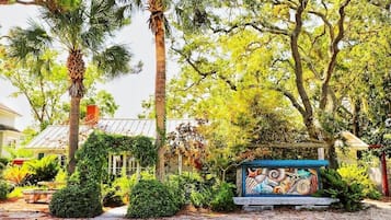 A garden with a palm tree, a mural, and a house with a metal roof.