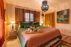 A well-appointed bedroom with a large bed, decorative pillows, a bedside table with a lamp, a tray of breakfast items, and a chandelier. - Creekside Paradise • Sunsets, Pool, Spa, Dock, Kayaks (Tybee Island)
