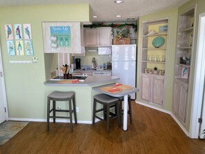 Uma cozinha com ilha central, banquetas de madeira, geladeira e cafeteira.