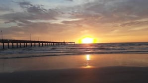 Solnedgang over en strand med en mole, der stikker ud i vandet.