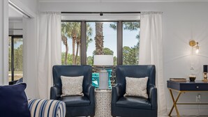Ein modernes Wohnzimmer mit zwei dunkelblauen Sesseln, einem gestreiften Sofa, einem kleinen runden Tisch und einem Schreibtisch mit einer Lampe.