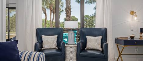 A modern living room with two dark blue armchairs, a striped sofa, a small round table, and a desk with a lamp.