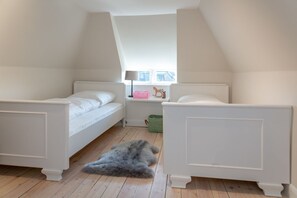 A bedroom with two white beds, a window with a view, a lamp, and a rug on the floor.