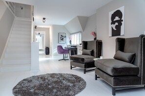 A modern living room with a staircase, grey sofas, a purple chair, and a large artwork on the wall.
