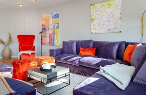 A modern living room with a purple sofa, red armchair, and orange ottoman. There is a coffee table in the center.