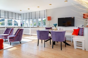 A modern living room with a large TV, purple chairs, a white sofa, and a dining table.