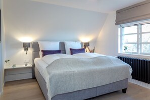 A bedroom with a large bed, two bedside tables, a nightstand, a window with a view, and a radiator.