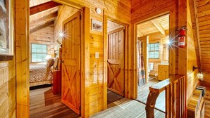A wooden cabin interior with a cozy bedroom, a bathroom, and a dining area.