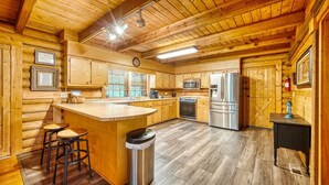 A wooden cabin interior with a kitchen featuring a central island, bar stools, a trash can, and a fire extinguisher.