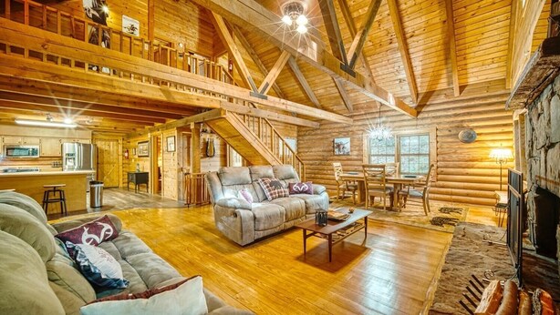 A spacious log cabin interior with a living room, dining area, kitchen, and a staircase leading to an upper level.