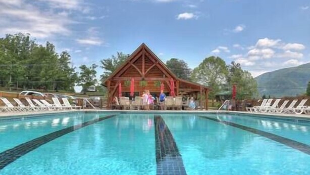 A swimming pool with lounge chairs and a wooden pavilion in the background.