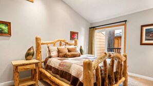 A rustic wooden bed with a quilt, a bedside table, and a lamp. - Summit Condo - Luxury Condo, Walk to Slopes, Fireplace (Big Bear Lake)