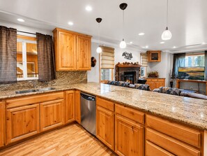 A kitchen with wooden cabinets, granite countertops, a dishwasher, and a fireplace.