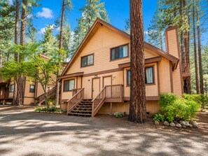 A two-story lodge with a wooden exterior, a front staircase, and a view of the surrounding forest.