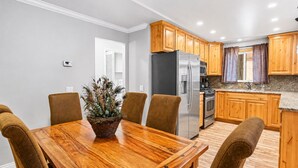 A modern kitchen with wooden cabinets, a stainless steel refrigerator, and a dining area with a wooden table and chairs. - Summit Condo - Luxury Condo, Walk to Slopes, Fireplace (Big Bear Lake)