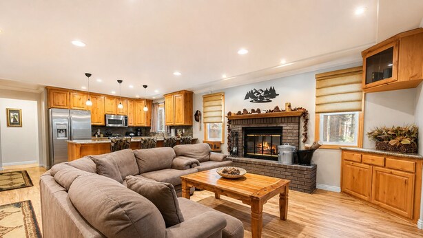 A modern living room with a sectional sofa, a fireplace, wooden cabinets, and a kitchen area with stainless steel appliances. - Summit Condo - Luxury Condo, Walk to Slopes, Fireplace (Big Bear Lake)