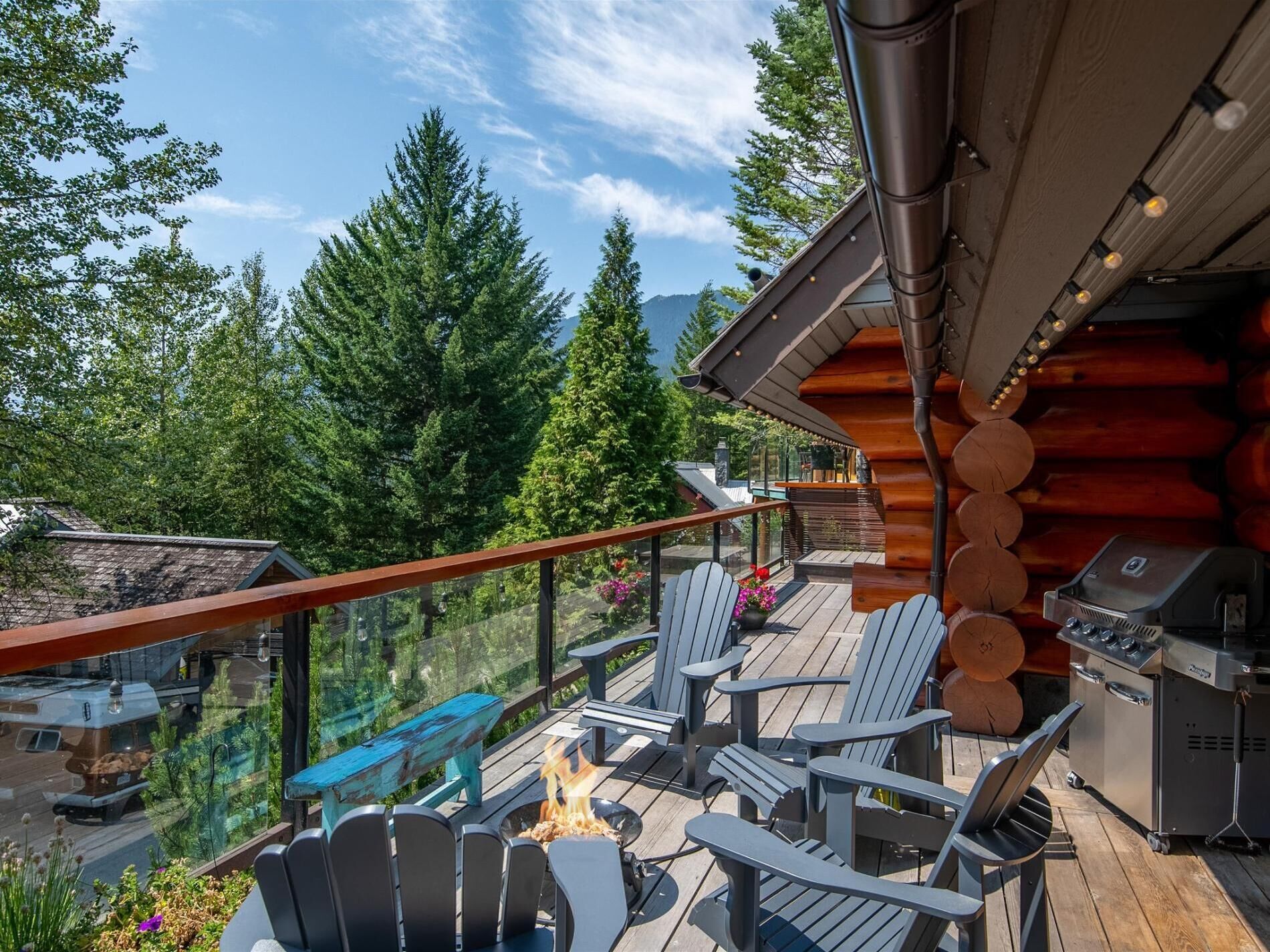 Une terrasse en bois avec des fauteuils Adirondack, un barbecue et un foyer extérieur.