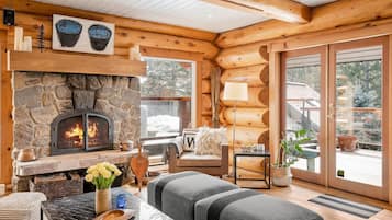 L’intérieur chaleureux d’un chalet en bois, avec une cheminée en pierre, un coin salon confortable et de grandes fenêtres donnant sur le paysage extérieur.