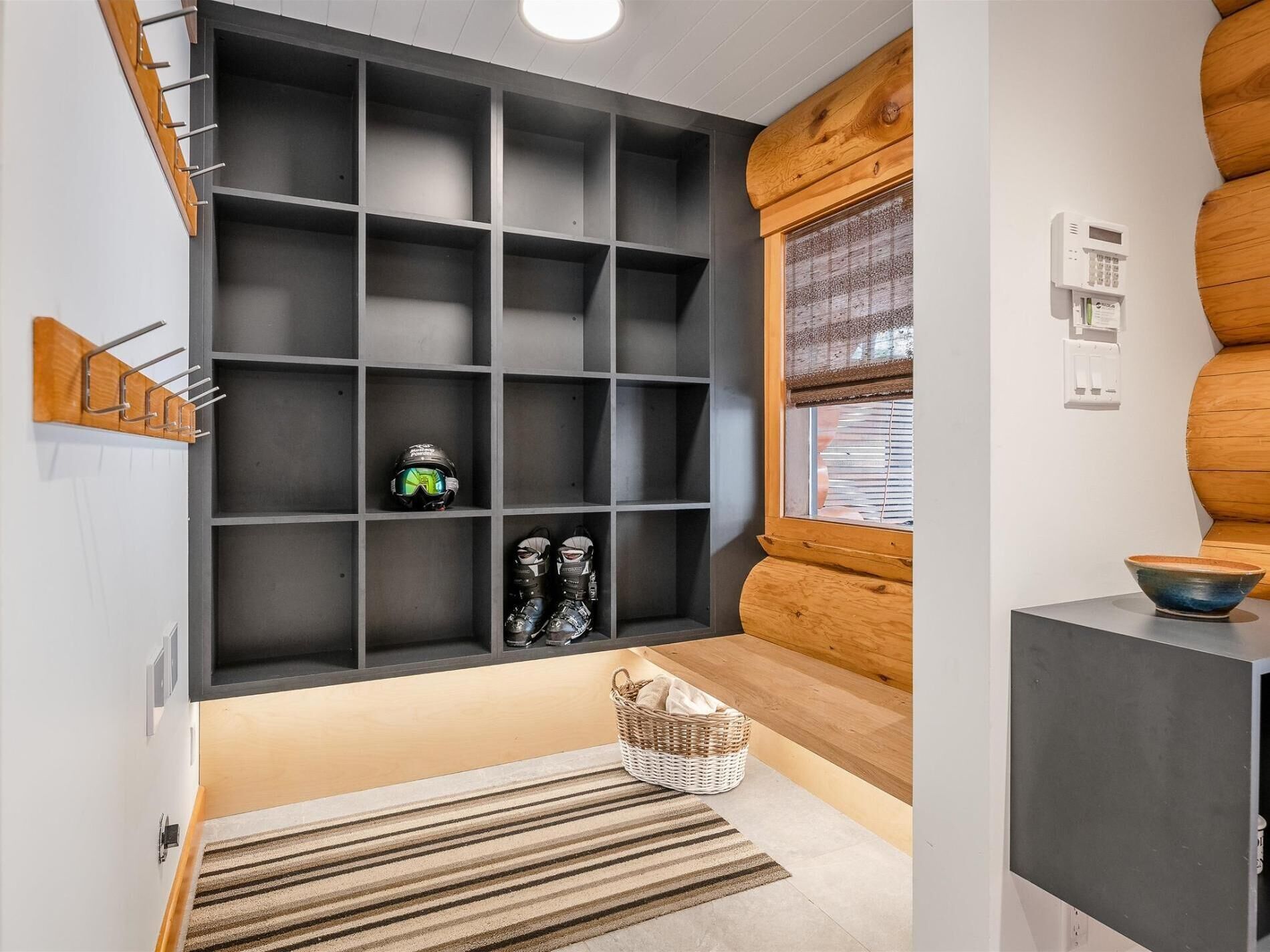 Un intérieur moderne avec une étagère grise, un mur en bois, une fenêtre avec des stores, une petite table sur laquelle se trouve un bol, et un panier en osier.