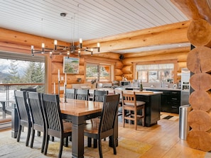 L’intérieur d’une cabane en rondins comprend un coin repas, une cuisine et de grandes fenêtres.