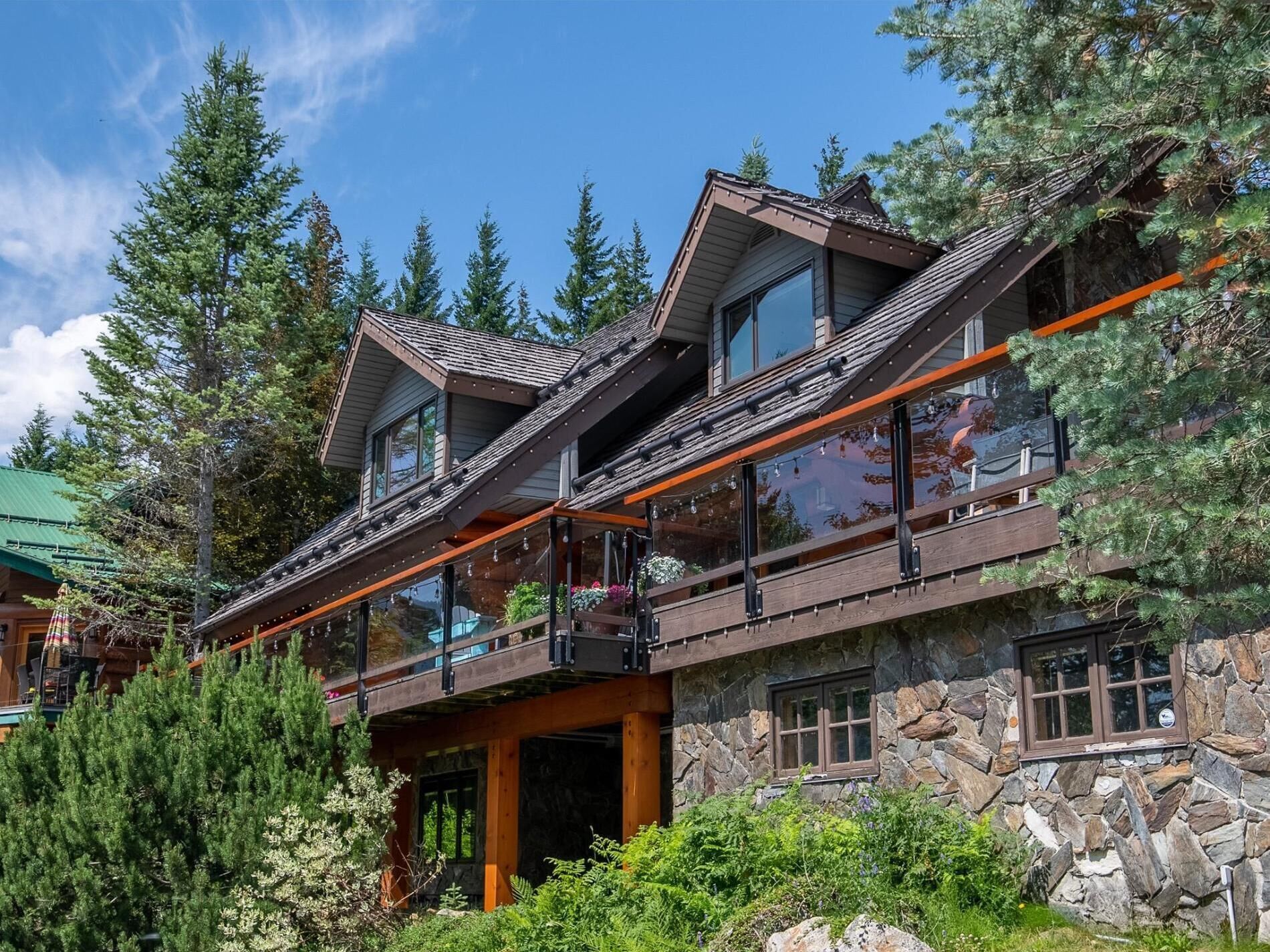 Une maison en pierre à plusieurs étages, dotée d’une terrasse en bois et de grandes fenêtres.