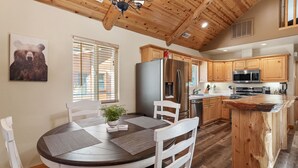 A kitchen with wooden cabinets, a stainless steel refrigerator, a microwave, and a wooden island with a sink.