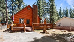 A rustic cabin with a wooden deck, a chimney, and a fenced yard.