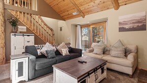 A cozy living room with a wooden staircase, two sofas with cushions, a coffee table, and a view of the outdoors through a glass door.