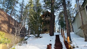 A snow-covered wooden staircase leading to a cabin surrounded by tall pine trees. - TreeHouse on Rainbow - Views, Fireplace, Deck, Barbecue (Big Bear City)